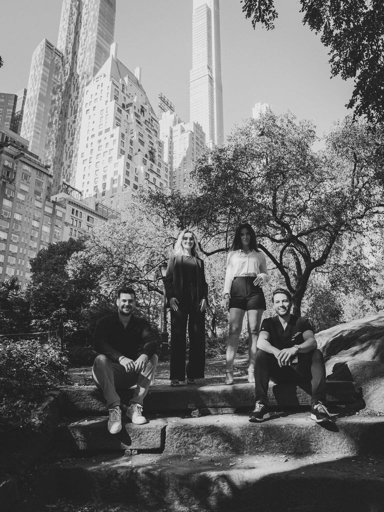 Four people sitting on stone steps in a park with tall buildings in the background